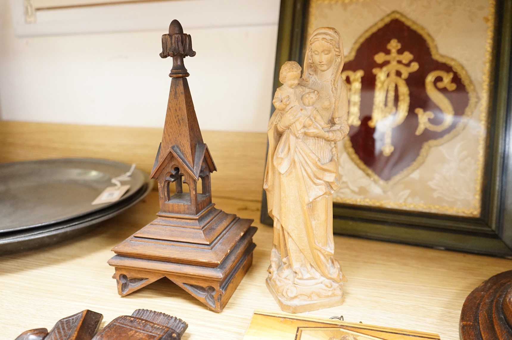 A pair of Gothic revival oak wall plaques, a Black Forest carved barometer, a Virgin and child figure, an IHS embroidered panel, two straw worked panels and a carved finial, barometer 47cm high